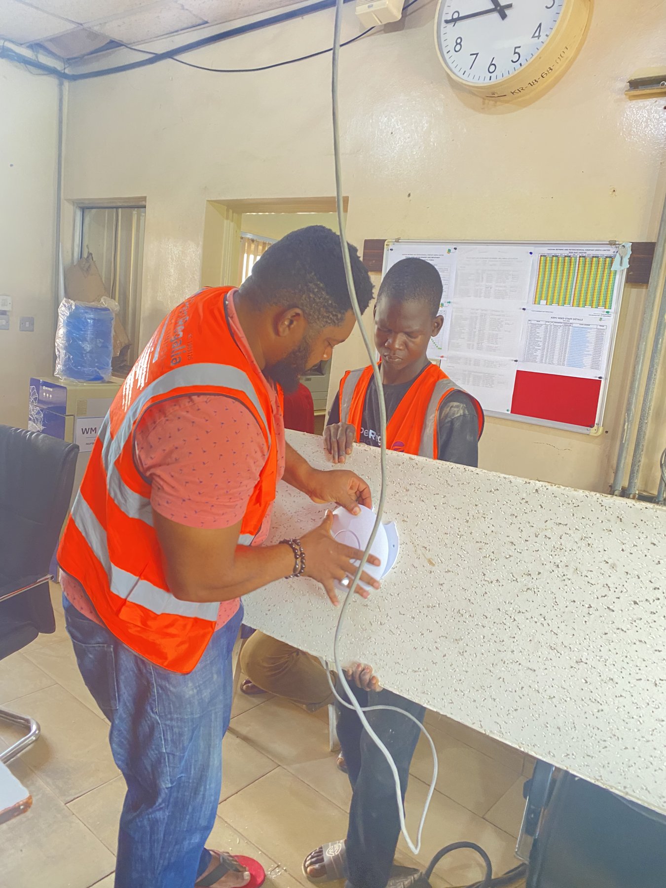 Technicians preparing a wireless access point and ceiling panel.